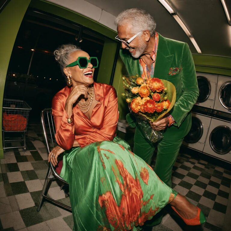 Older couple in green and coral eveningwear laughing with a bouquet of flowers in a green laundromat.